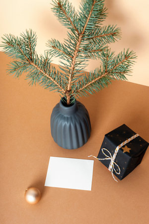 Spruce branch in ceramic vase, gift box and blank card on beige table. Minimal Christmas concept. Top view, mockupの写真素材