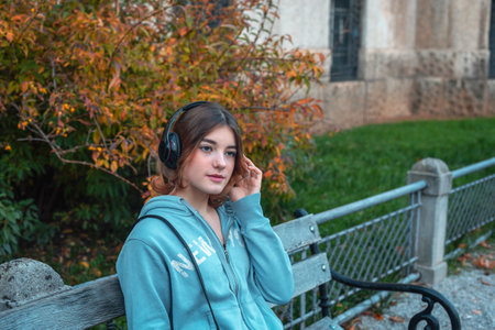 Beautiful young girl in headphones sitting on a benchの写真素材