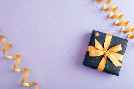 Gift box and golden tinsel on purple background with confetti. Christmas, New Year or birthday concept. Top view, flat lay, copy space.の写真素材