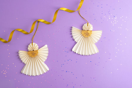 Two Christmas paper angels with golden tinsel on purple background. Christmas holiday concept. Top view.の写真素材