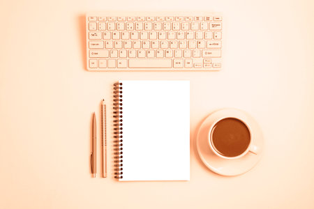 Workplace with computer keyboard, notepad, pen, pencil and cup of coffee or cocoa on peachy background. Top view, flat lay, mockup. Image toned in trendy color of year 2024 Peach Fuzzの写真素材