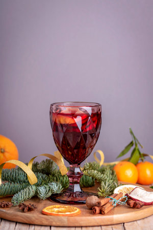 Wineglass with mulled wine on wooden tray with fruits and Christmas decorations on gray background. Closeup, copy space.の写真素材