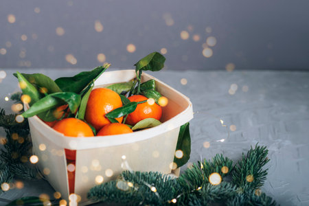 Tangerines in a basket with christmas lights on gray background.の写真素材