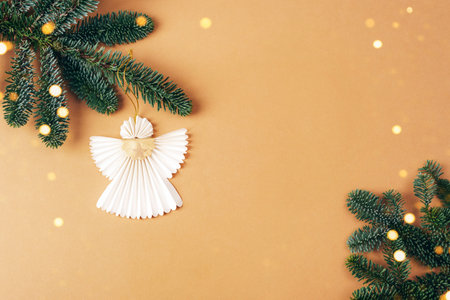 Christmas paper angel hanging on the fir tree branch on beige background. Christmas holiday concept. Top view, flat lay.の写真素材
