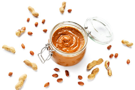 Peanut butter in a jar with scattered peanuts isolated on white background. Vegan food. Top viewの写真素材