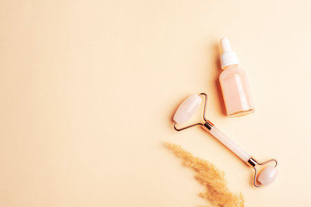 Pink serum bottle, rose quartz crystal facial roller and pampas grass on neutral beige background. Top view, flat lay, copy space.の写真素材
