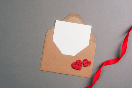 Envelope with blank card, red hearts and ribbon on gray background. Valentines day concept, top view, flat lay, mockup.の写真素材