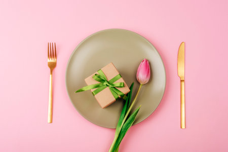 Gift box and pink tulip flower on light green plate on pink background Mothers day, womens day concept. Top view, flat lay.の写真素材