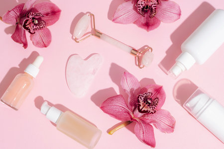 Facial cosmetic roller and gua sha scraper with pink orchid flowers and serum bottles. Sharp shadows. Home spa concept. Top view, flat lay.の写真素材