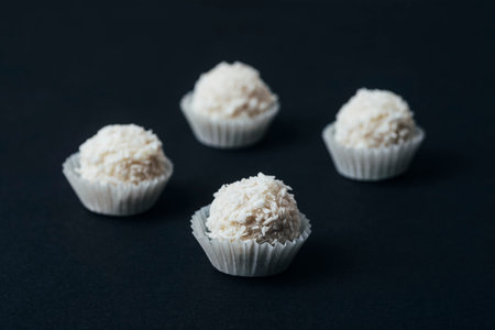 Coconut candies in paper cups on black table. Closeup.