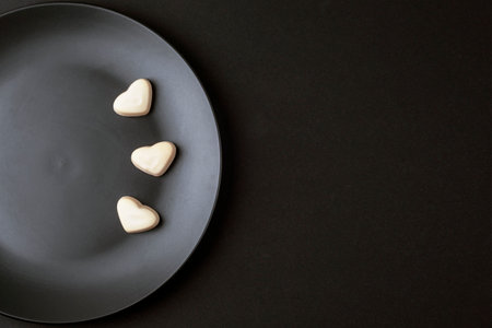 Three heart shaped candies on black plate. Top view, flat lay, copy spaceの写真素材