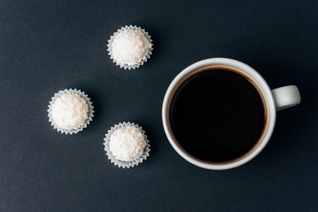 Coffee cup and coconut candies on black table. Top view, flat layの写真素材