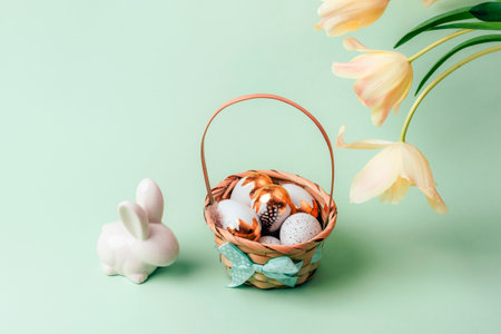 Basket with painted white and golden eggs, bunny and yellow tulips on light green background. Easter concept. Closeupの写真素材