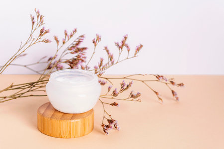 Cosmetic cream in a jar and purple kermek flowers on beige table. Natural cosmetics concept. Closeup.の写真素材