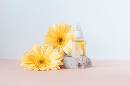 Cosmetic serum bottle on stone podium with yellow gerbera flowers on beige and white background. Front view.の写真素材