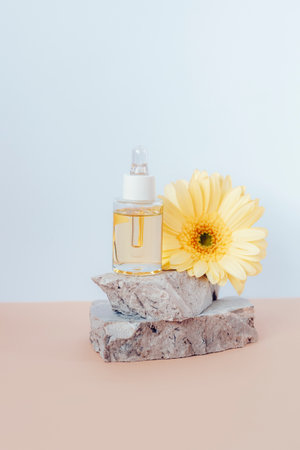 Cosmetic serum bottle on stone podium with yellow gerbera flower on beige and white background. Front view.の写真素材
