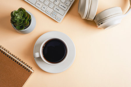 Desktop with notepad, computer keyboard, headphones, succulent plant and coffee cup on beige background. Top view, flat lay, copy space.の写真素材