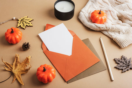 Autumn flat lay with envelope with envelope with blank card, pumpkins, yellow leaves and candle on neutral background. Mockupの写真素材
