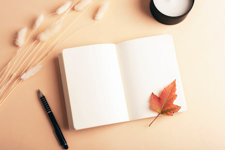 Blank open notepad, pen, bunny tails grass, autumn leaf and candle on beige background. Top view, flat lay, mockupの写真素材