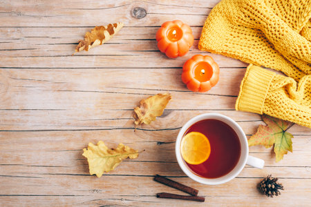 Autumn aesthetic concept. Cup of tea, candles, autumn leaves and yellow sweater on wooden background. Top view, flat lay, copy spaceの写真素材