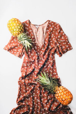 Brown floral summer dress and pineapples on white background. Flat lay, top viewの写真素材