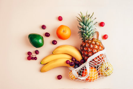 Pineapple, banana, oranges, avocado and grapes in a string bag. Zero waste concept, healthy food. Top view, flat layの写真素材
