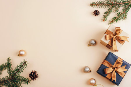 Minimal Christmas flat lay with fir branches, gift boxes tied with golden ribbons and festive ornaments on a beige background. Top view, copy spaceの写真素材