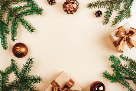 Christmas-themed composition with green pine branches, bronze gift boxes with ribbons, and ornaments arranged on a beige background. Top view, flat layの写真素材