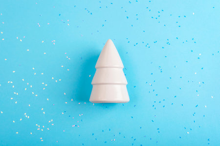 White ceramic Christmas tree surrounded by confetti on a light blue background, top viewの写真素材
