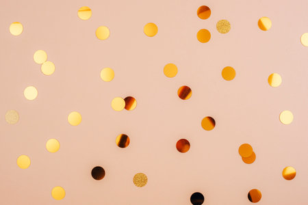 Golden confetti scattered on a soft beige background, top viewの写真素材
