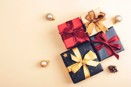 Multiple wrapped gift boxes with golden and red ribbons on a light background, surrounded by baubles...