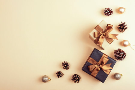 Elegant gift boxes with golden ribbons surrounded by pine cones and festive baubles on a beige background, creating a warm holiday aesthetic. Top view, flat lay, copy spaceの写真素材