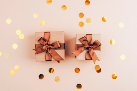 Minimalistic gift boxes with brown ribbons and golden confetti scattered on a beige background for a festive celebration. Top view, flat lay, copy spaceの写真素材