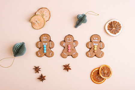 Gingerbread cookies arranged with dried orange slices, star anise, and holiday ornaments on a beige background. Top view, flat lay.の写真素材