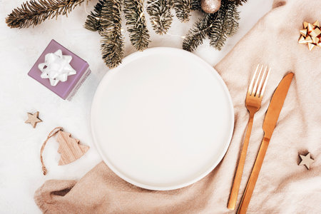 Flat lay of festive table setting with blank plate, gold cutlery, pine branches, and Christmas decorations. Top view, copy space.の写真素材