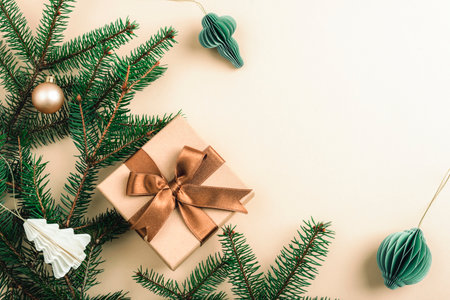 Christmas flat lay with green fir branches, a wrapped gift with a brown bow, and paper ornaments on a beige background. Top view, copy space.の写真素材