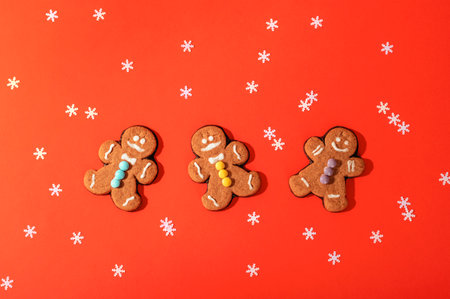 Gingerbread cookies on orange background with scattered white snowflakes for a festive holiday atmosphere. Christmas concept. Top view, flat lay.の写真素材