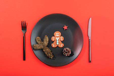 Gingerbread cookie styled on a black plate with a festive red background and minimal decor. Top view, flat layの写真素材