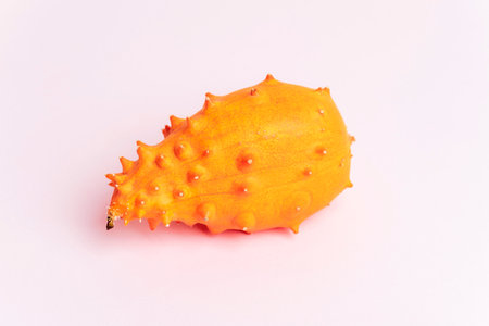 Vibrant horned melon with spiky orange skin on a soft pink background. Kiwano fruit, closeup.の写真素材