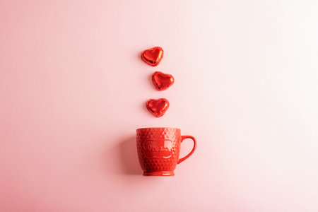 Red ceramic mug with heart-shaped chocolates on a pastel pink background. Valentines day concept. Top view, flat lay.の写真素材