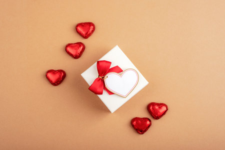Gift box with a red bow and heart-shaped chocolates on a brown background. Valentine's Day celebration. Top view, flat lay, mockup.の写真素材