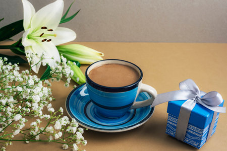 Cup of coffee with white lilies, baby breath flowers, and a small blue gift box with a ribbon. Womens day, Valentines day, spring holiday concept.の写真素材
