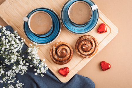 Two cups of coffee with cinnamon rolls, heart-shaped chocolates, and white flowers on a wooden board. Valentines day concept. Top view, flat lay.の写真素材