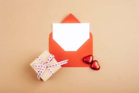 Red envelope and small gift box with heart-shaped decorations on a beige background, symbolizing love. Valentines day concept. Top view, flat lay, mockup.の写真素材