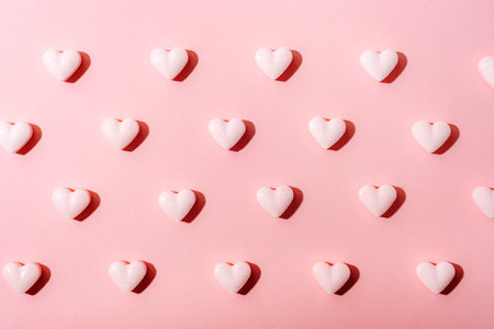 White heart-shaped candies with sharp shadows arranged in a grid on a pink background, symbolizing sweetness and love. Texture, background.の写真素材