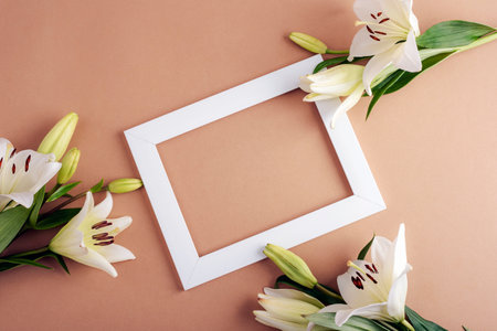 White lilies and a white rectangular picture frame on a beige background, symbolizing elegance, purity, and romantic decoration. Top view, flat lay, mockup.の写真素材