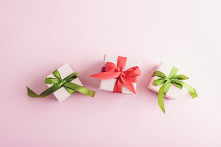 Three small gift boxes with green and red ribbons on a pastel pink background. Top view, flat lay.の写真素材