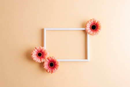 White empty frame decorated with pink gerbera flowers on a beige background. Top view, flat lay,...