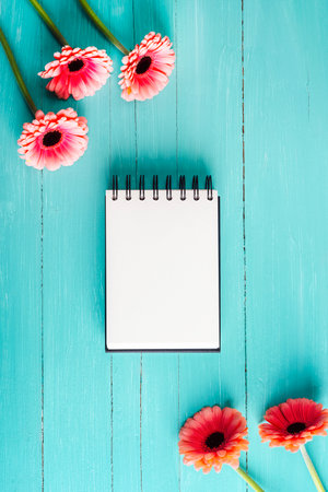 Blank notepad with pink gerbera flowers on a turquoise wooden background. Top view, flat lay, mockupの写真素材