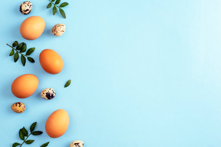 Brown and quail eggs with green leaves on blue background. Easter concept. Top view, flat lay, copy spaceの写真素材